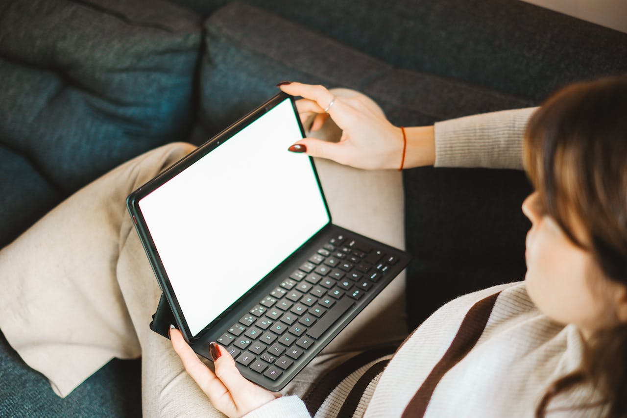 A woman uses a tablet with a keyboard on a comfortable sofa, emphasizing remote work flexibility.